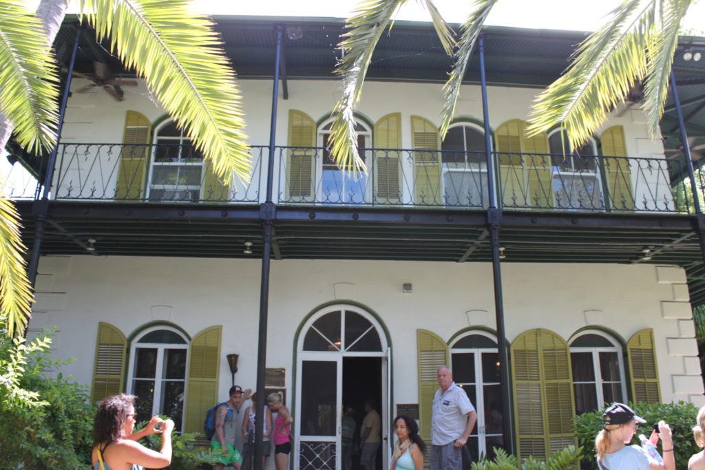 A white stone building with a metal upper porch and green shutters flanked by palm trees at Ernest Hemingway Home & Museum in Key West